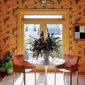 A marigold interior with floral yellow wallpaper, yellow trim, leather chairs, and a big potted plant in the middle on a table.