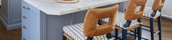 A close up of three counter stools with square backs made from rush and striped cushions, in a kitchen scene.