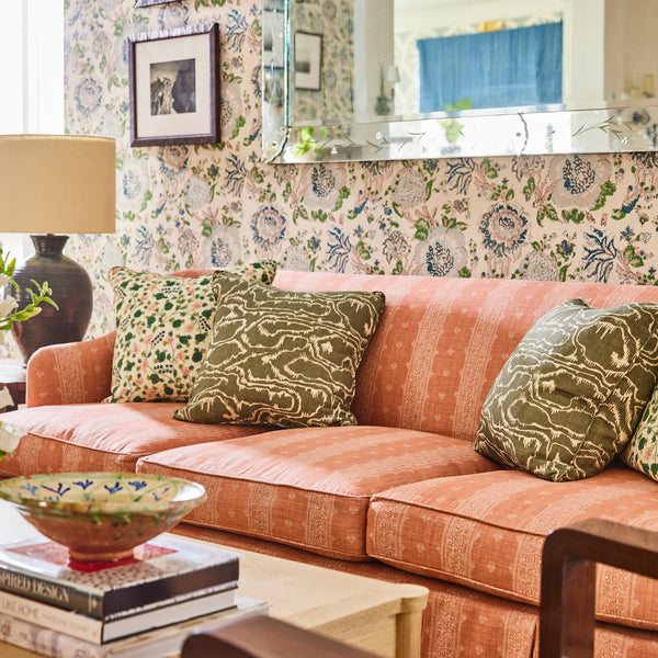 Orange patterned sofa with rolled arms, styled with green and floral throw pillows.