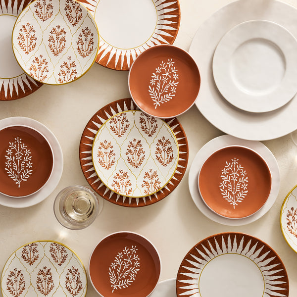 Orange appetizer plate with white floral tree motif, placed among matching dishes