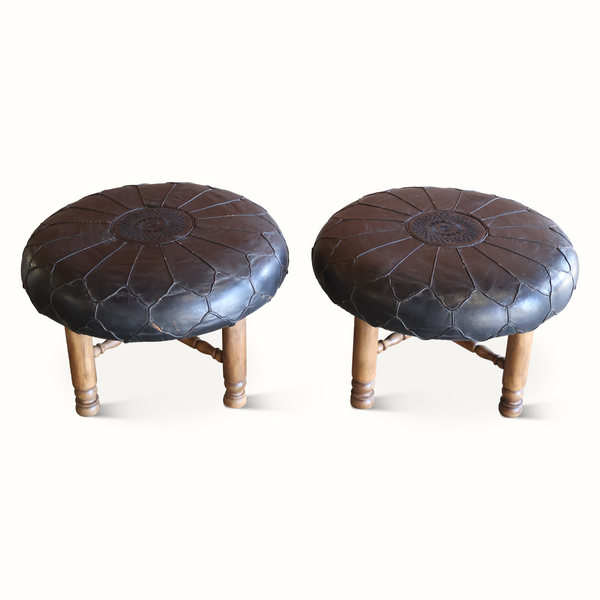 Pair of round ottomans with dark tufted leather tops and carved wooden legs