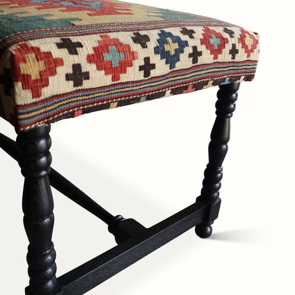 Close-up of kilim bench seat edge with multicolor geometric woven pattern on dark wood leg