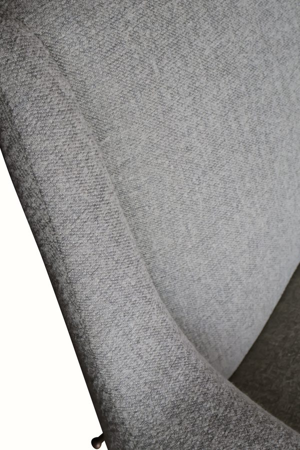 Gray textured upholstery close-up on a curved armrest of a mid-century settee.