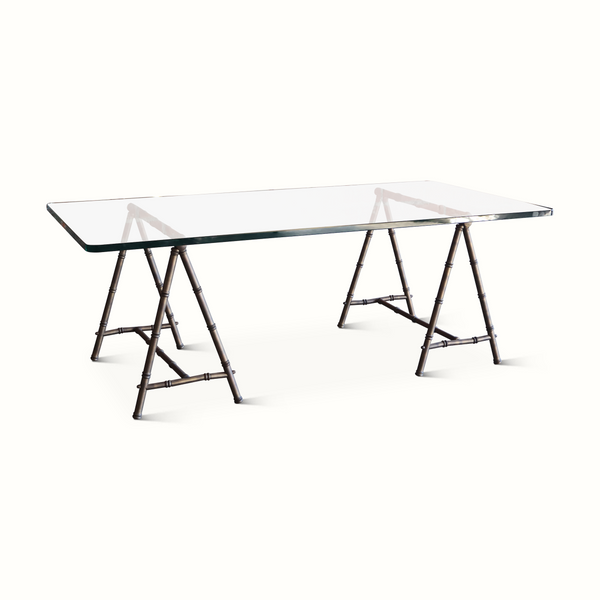 Wide view of coffee table with clear glass top and dark metal bamboo-style trestle frame