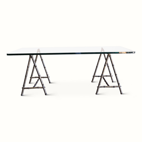 Coffee table from side angle with clear glass top and bamboo-style trestle legs