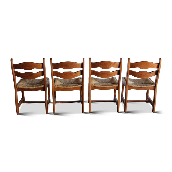 Set of four wooden dining chairs with wavy back slats, armrests, and textured seat cushions