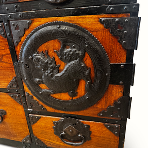 Wooden tansu chest drawer front with dragon relief knob and ornate metal trim.