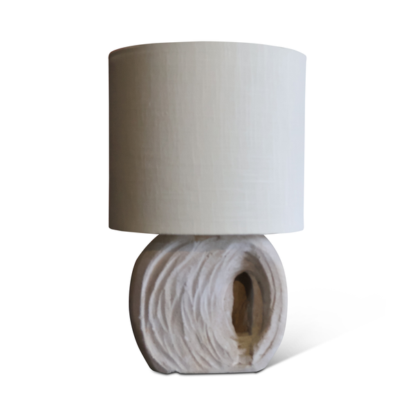 Table lamp with light fabric drum shade and rolled stone base with cutout window