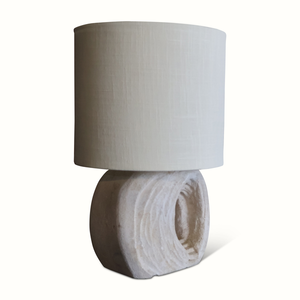 Table lamp with light fabric drum shade and textured round stone base, side view