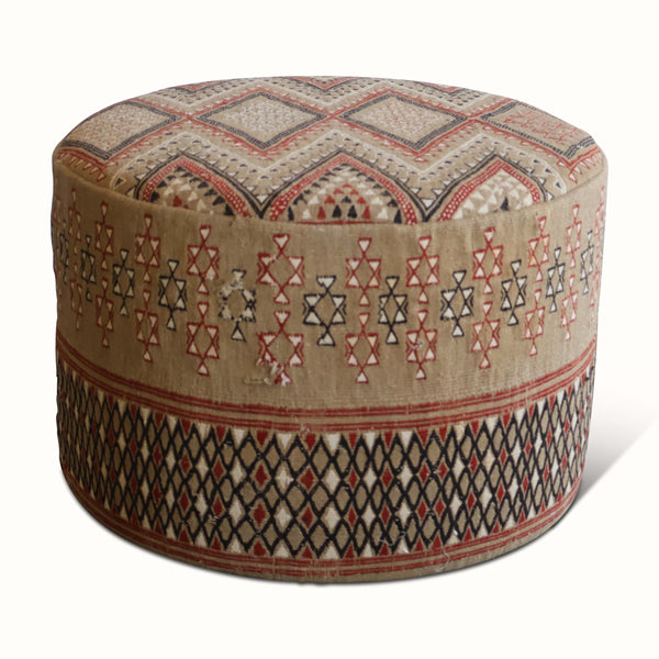Round upholstered ottoman with vintage Moroccan rug pattern, beige base and red/blue accents.