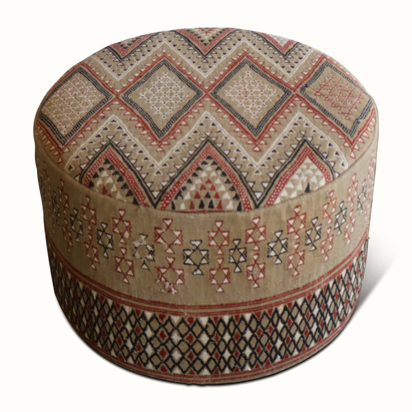 Round upholstered ottoman with patterned sides and top, beige fabric with red and navy shapes.
