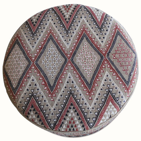 Round ottoman top, beige Moroccan rug design with red, navy, and gray diamond motifs.