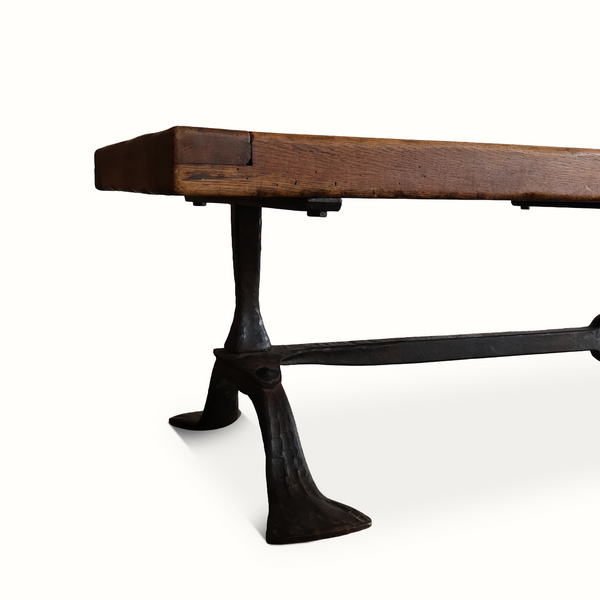 Coffee table side view with rustic oak top and dark forged iron pedestal base.