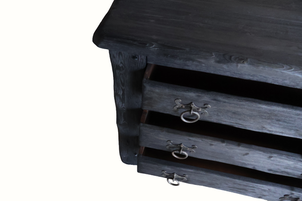 Close-up of ebonized oak chest drawers with ornate metal knobs, dark distressed wood