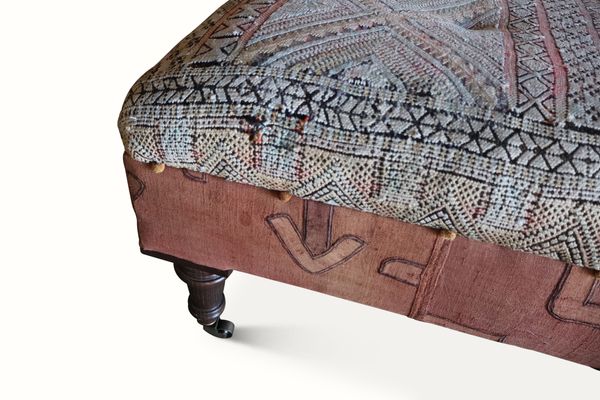 Tufted ottoman corner detail with patterned fabric top and dark carved wood leg