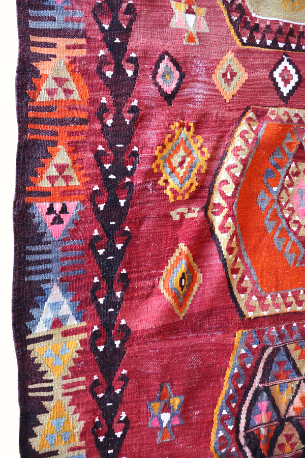 Turkish kilim rug close-up, burgundy fabric with navy diamonds, orange stripes and small motifs.