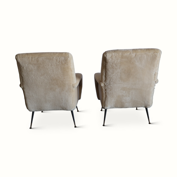 Pair of sheepskin armchairs, rear view, cream upholstery panels and curved armrests, black legs