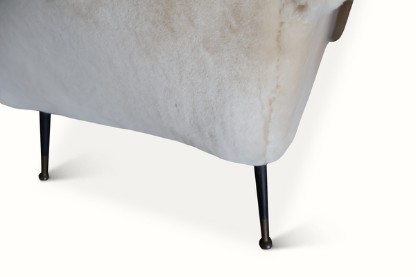 Sheepskin armchair base close-up, cream seat edge with black legs and rounded feet