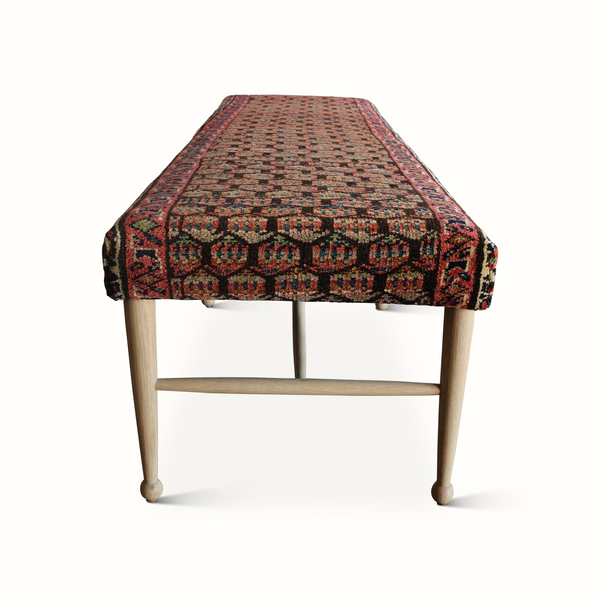 Bench with red-and-brown geometric rug cover over light wood frame, curved legs