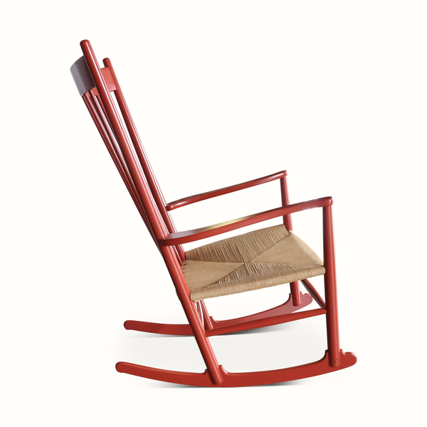 Red wooden rocking chair side view with curved rockers and woven beige seat