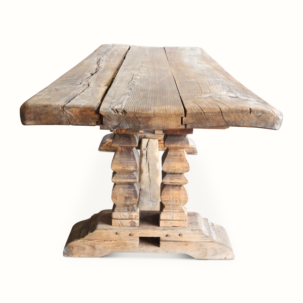 Weathered farm table with large rectangular top and sculpted pedestal legs