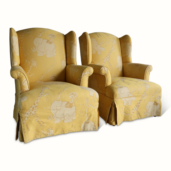 Pair of yellow wingback armchairs angled view, upholstered with light animal circus print