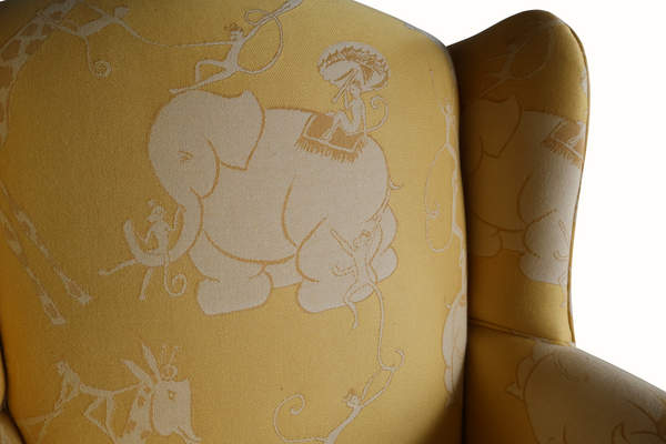 Yellow wingback armchair backrest detail with light animal circus print on upholstered fabric