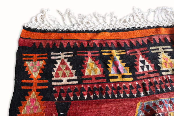 Turkish kilim rug edge, black ground with orange trim, repeating geometric figures and fringe.