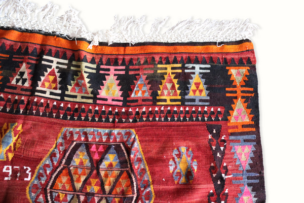 Turkish kilim rug corner, black band with orange and yellow motifs, white fringe tassels.
