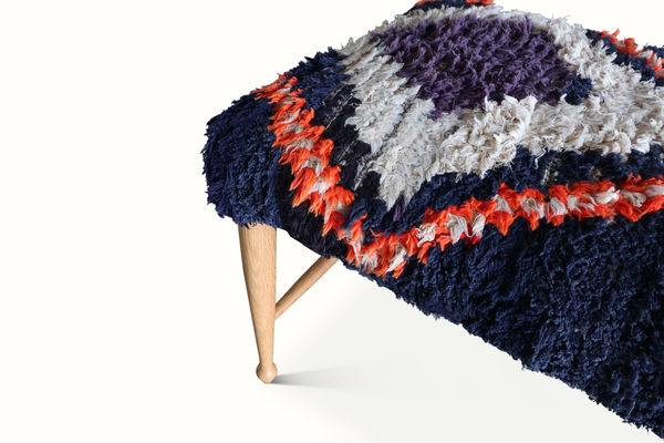 Rug-covered bench end view: navy shag with orange accents and white stripe