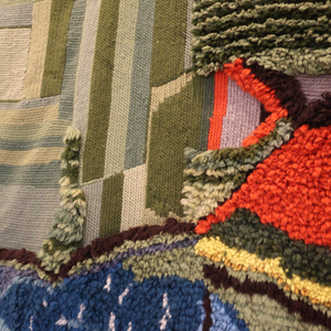 Woven landscape tapestry close-up with green blocks, orange path, multicolor fringed trim