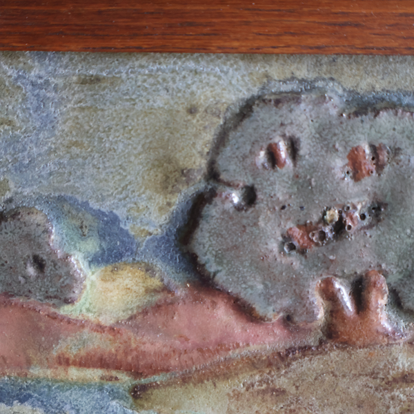Close-up of scenic pottery tile surface, textured gray-and-pink landscape with raised accents