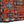 Close-up of orange rug with diamond and cross patterns, dark border, fringed edge