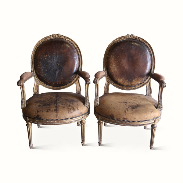 Pair of round-back upholstered armchairs with dark leather-look seats and gilded frames