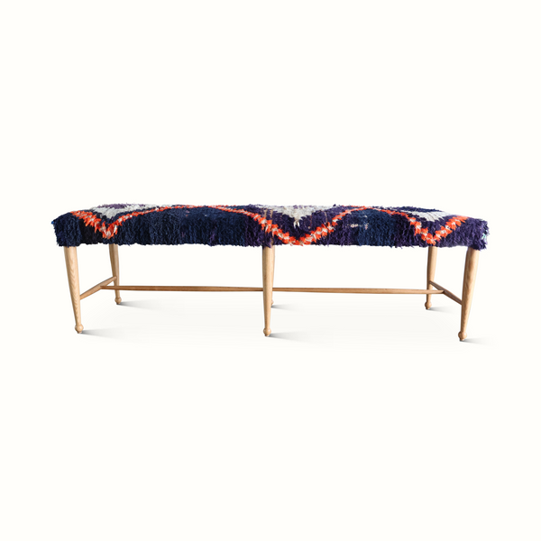 Moroccan rug bench with navy-and-orange fringed cushioned top and light wood legs