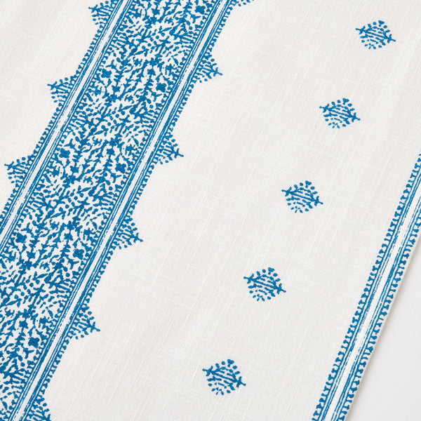 White runner rug with scattered blue medallion motifs and blue tassel trim along edge