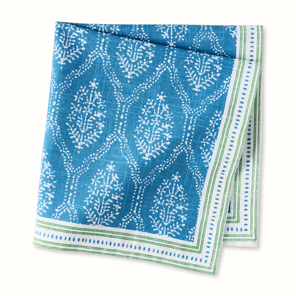Blue printed fabric napkin with white motif and green border, folded square.