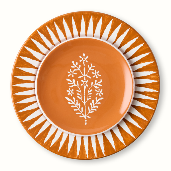 Orange appetizer plate with white floral tree motif, nested in striped sunburst plate