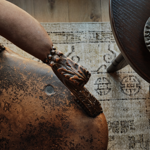 Detail of carved wooden arm and dark leather-look armchair upholstery with decorative trim