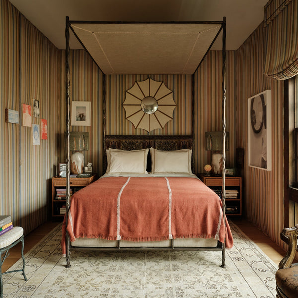 Four-poster canopy bed with dark posts, cream pillows, coral pink throw blanket