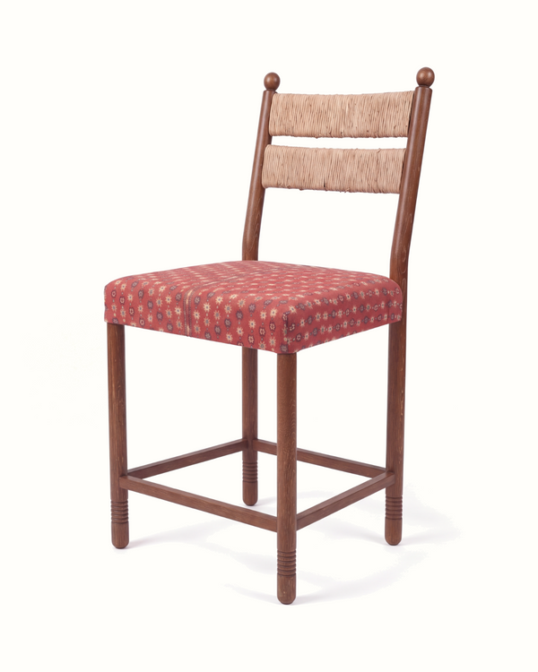Counter-height upholstered stool with woven rush back, red patterned seat, and cross brace