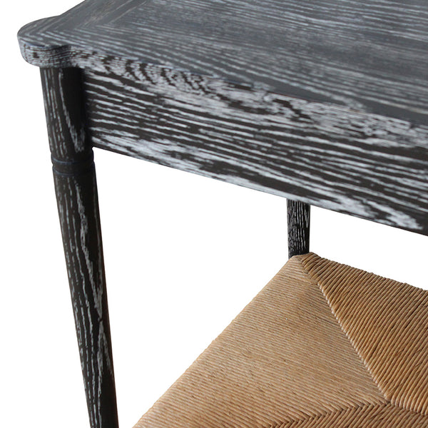 Black console table edge with woven paper rush shelf and visible distressed grain.